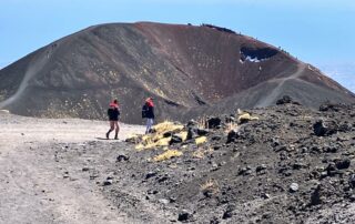 The image show two people hiking Etna and walk towards a huge crater - photo taken by Geo Etna Explorer - Etna Guided Tours