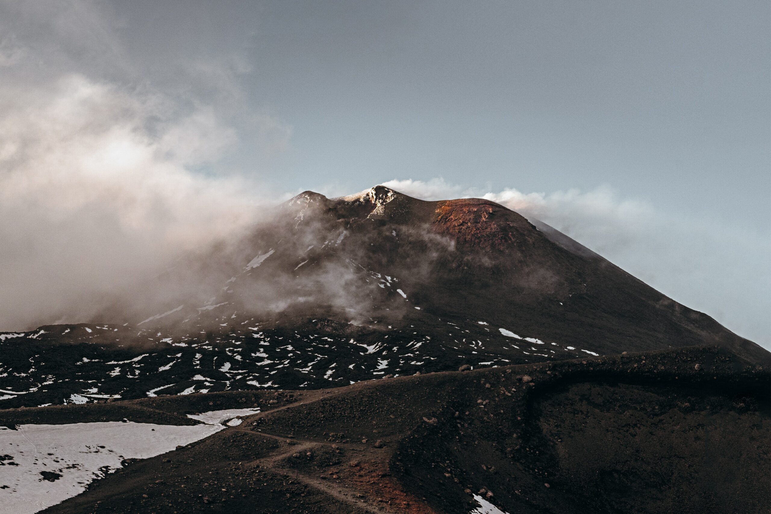 photo taken by Asa Roger showing Etna partially wrapped in smoke and clouds and you can clearly see the lava fields of past eruptions - photo used by Geo Etna Explorer Private and Group Tours Guided Jeep Excursions on Etna and Eastern Sicily
